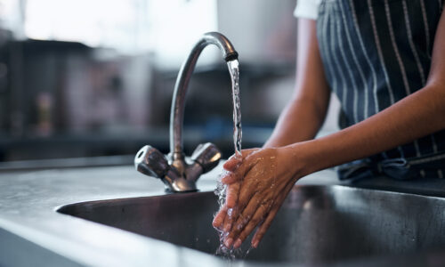 Cropped shot of a  woman washing her hands in the sink of a commercial kitchen.